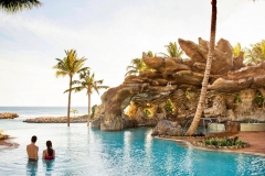 Ein Paar genießt den verlassenen Pool mit Felsformation und Palmen in Aulani