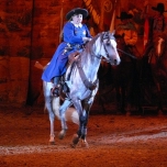 Annie Oakley in einem blauen Mantel sitzt auf einem Pferd