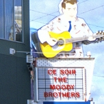 Werbetafel mit einem Gitarrenspieler und darunter die Aufschrift "Heute Abend: Moofy Brothers"
