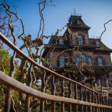 Phantom Manor hinter einem leicht verostet wirkenden Zaun, an dem sich Ranken winden