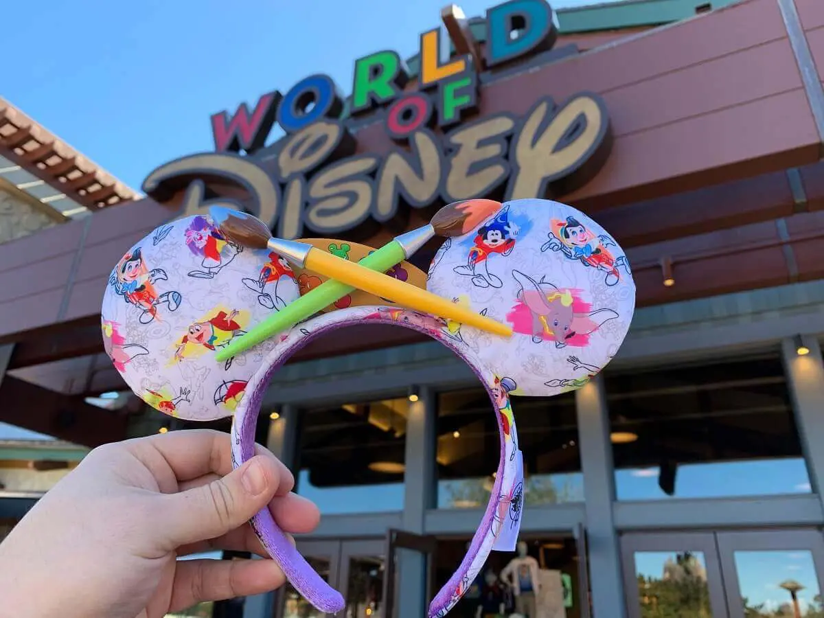 Ink and Paint Haarreifen Eine Hand hält ein Paar farbenfrohe Mickeyohren im "Ink & Paint"-Design vor dem World of Disney Store in Disney Springs in die Höhe