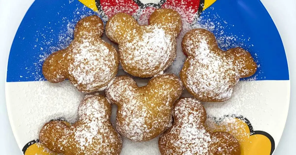 Sechs Beignets in Form eines Mickey Mouse Kopfes auf einem Teller im Donald Duck Design