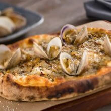 Auf einem Holztablett liegt ein Flatbread mit weißen Muscheln