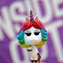 ein Funko Pop des Regenbogen-Einhorns aus dem Film "Alles steht Kopf" steht vor einem lilafarbenen Hintergrund