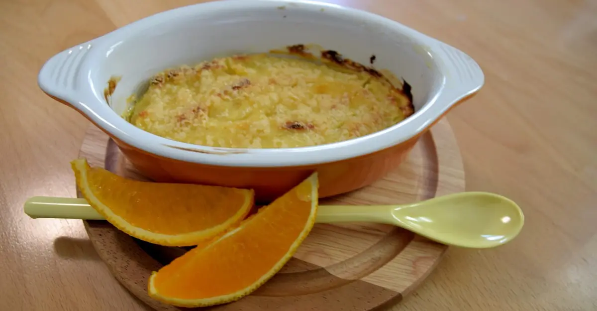 Auf einem kleinen runden Holztablett liegen eine kleine Schale mit Crema Catalana, ein langer Dessertlöffel und Orangenspalten