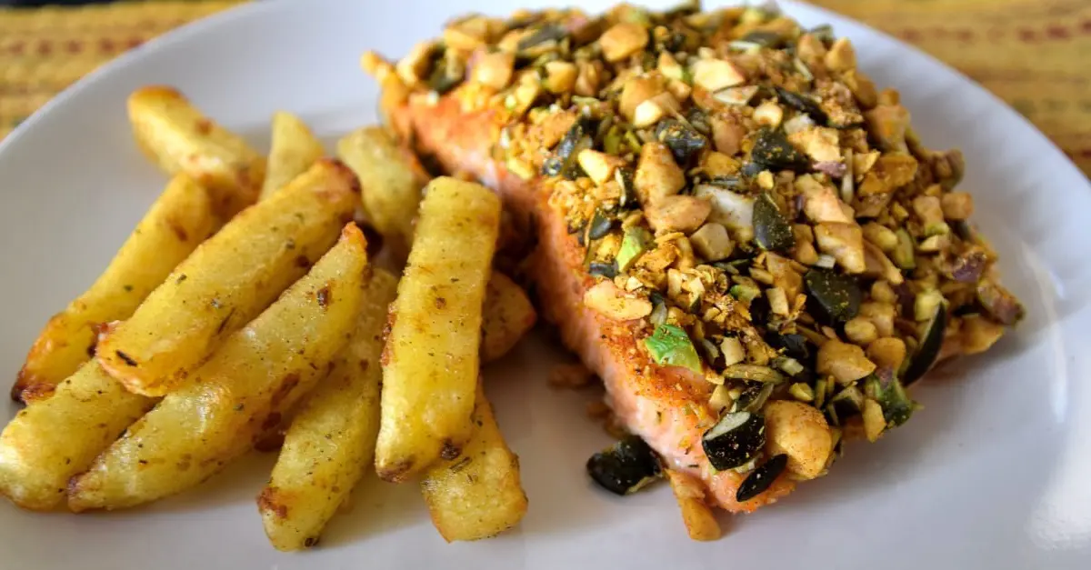 Nut Crusted Salmon Auf einem Teller liegen ein Stück Lachs mit Nusskruste und daneben mediterrane Pommes