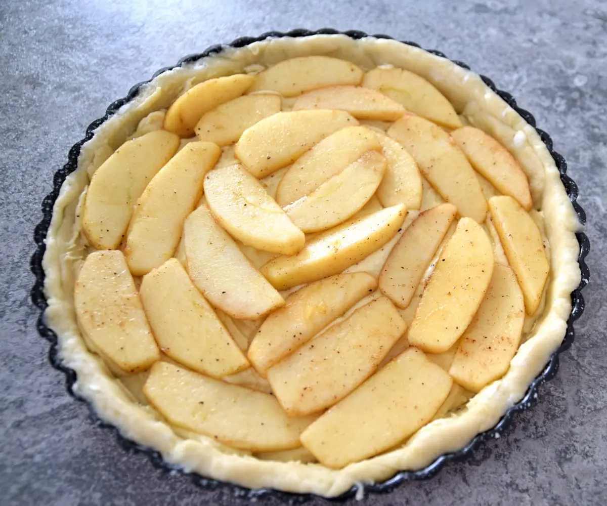 Tortenboden mit Apfelstücken In einer Tarteform befinden sich der Teig und die gedämpften Apfelscheiben für den Apfelkuchen