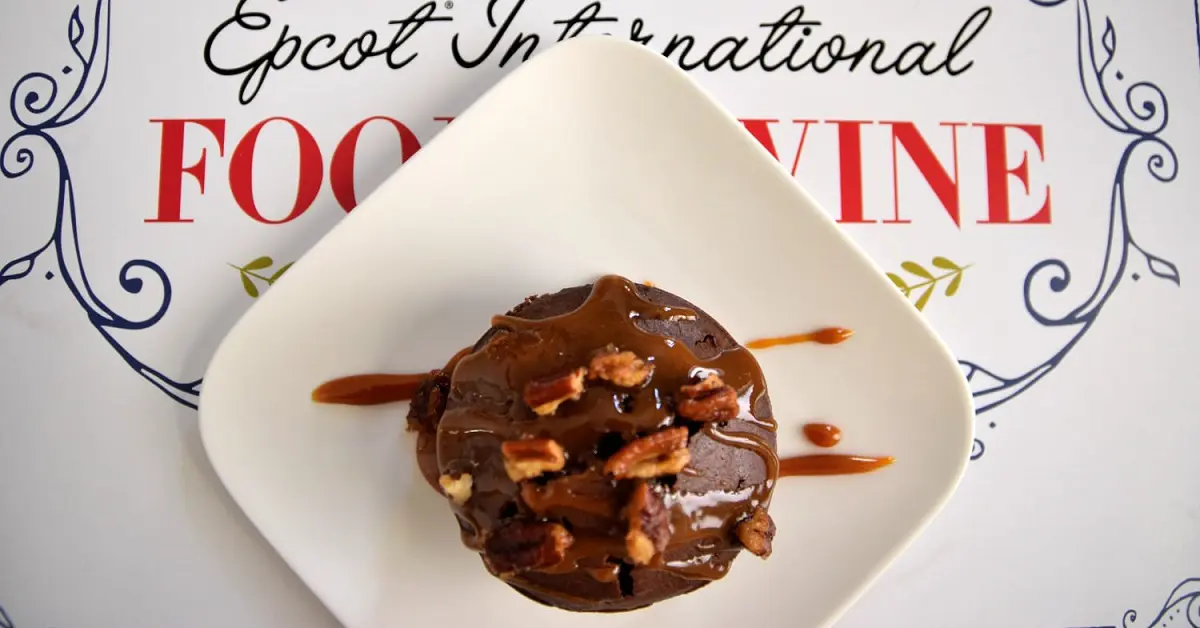 Warm Chocolate Cake Auf einem kleinen quadratischen weißen Teller ist ein Schokoküchlein mit Karamellsauce und Pekannüssen zu sehen