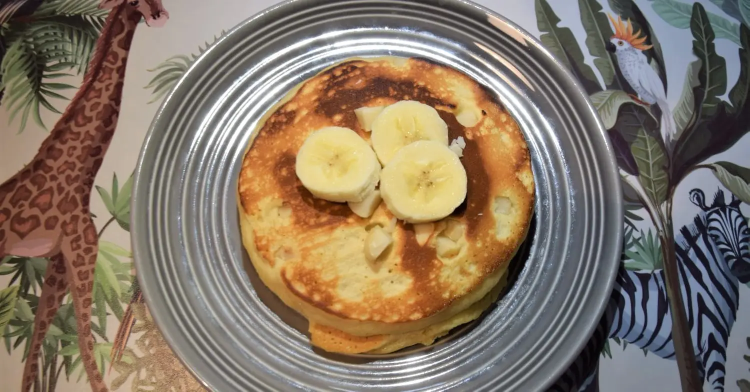 Pancakes mit Bananenscheiben Auf einem grauen Teller liegt ein Stapel von Pancakes mit Macadamianüssen und Bananenscheiben obenauf