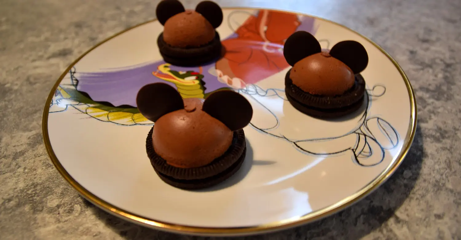 Mickey Mousse Domes Auf einem Teller mit Fantasia-Motiv liegen drei Mickey Mousse Domes nach einem Rezept aus dem Chef Mickey's in Walt Disney World