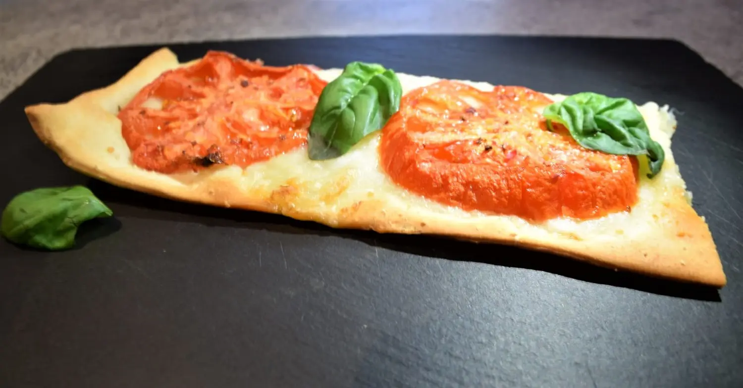 Tomaten Flatbread mit Basilikum Auf einer Schieferplatte liegt ein Stück Tomaten-Flatbread mit frischem Basilikum
