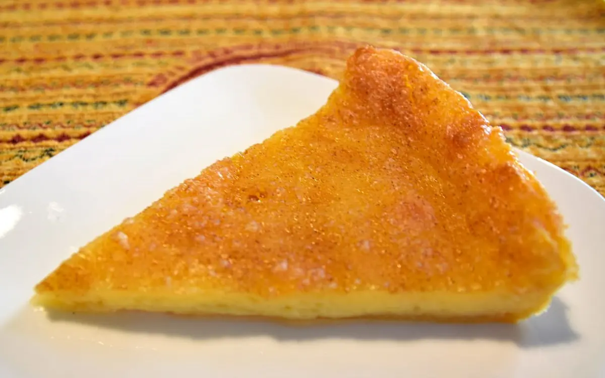 Ein Stück Melktert Auf einem kleinen weißen Teller liegt ein Stück der frisch gebackenen Melktert mit Zimt-Zucker-Topping