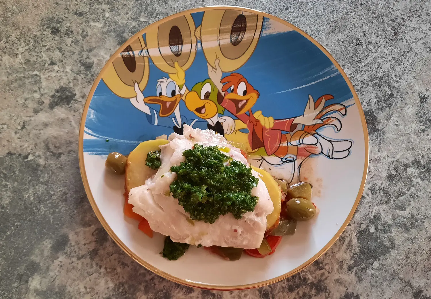 Eine Portion Pescado a la Veracruzana Auf einem Teller mit einem Bild der Drei Caballeros ist ein Stück Fisch auf Kartoffeln und Tomatensoße angerichtet