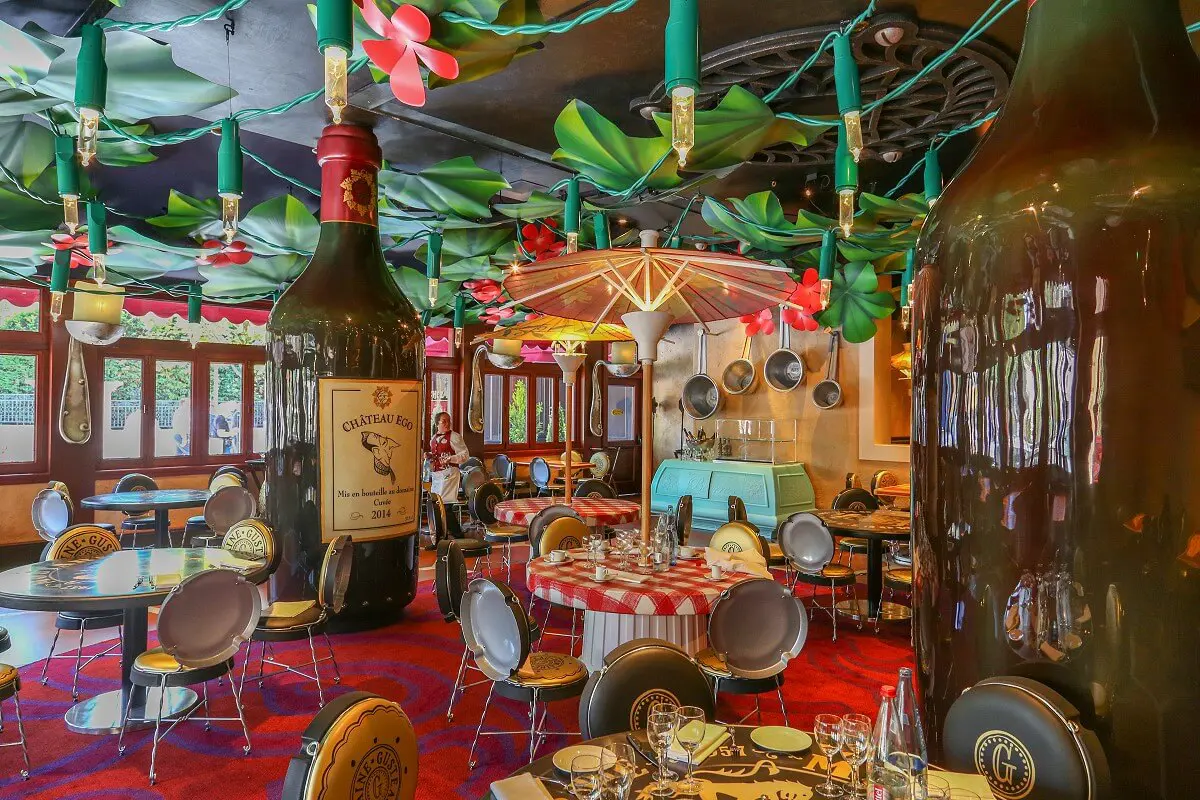Gastraum des Chez Remy Der Essbereich des Restaurant Chez Rémy mit übergroßen Flaschen als Säulen und Tischen und STühlen aus Flaschendeckeln.