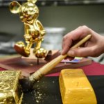Pinsel vergoldet einen Gipsbarren, im Hintergrund eine goldene Mickey Statue