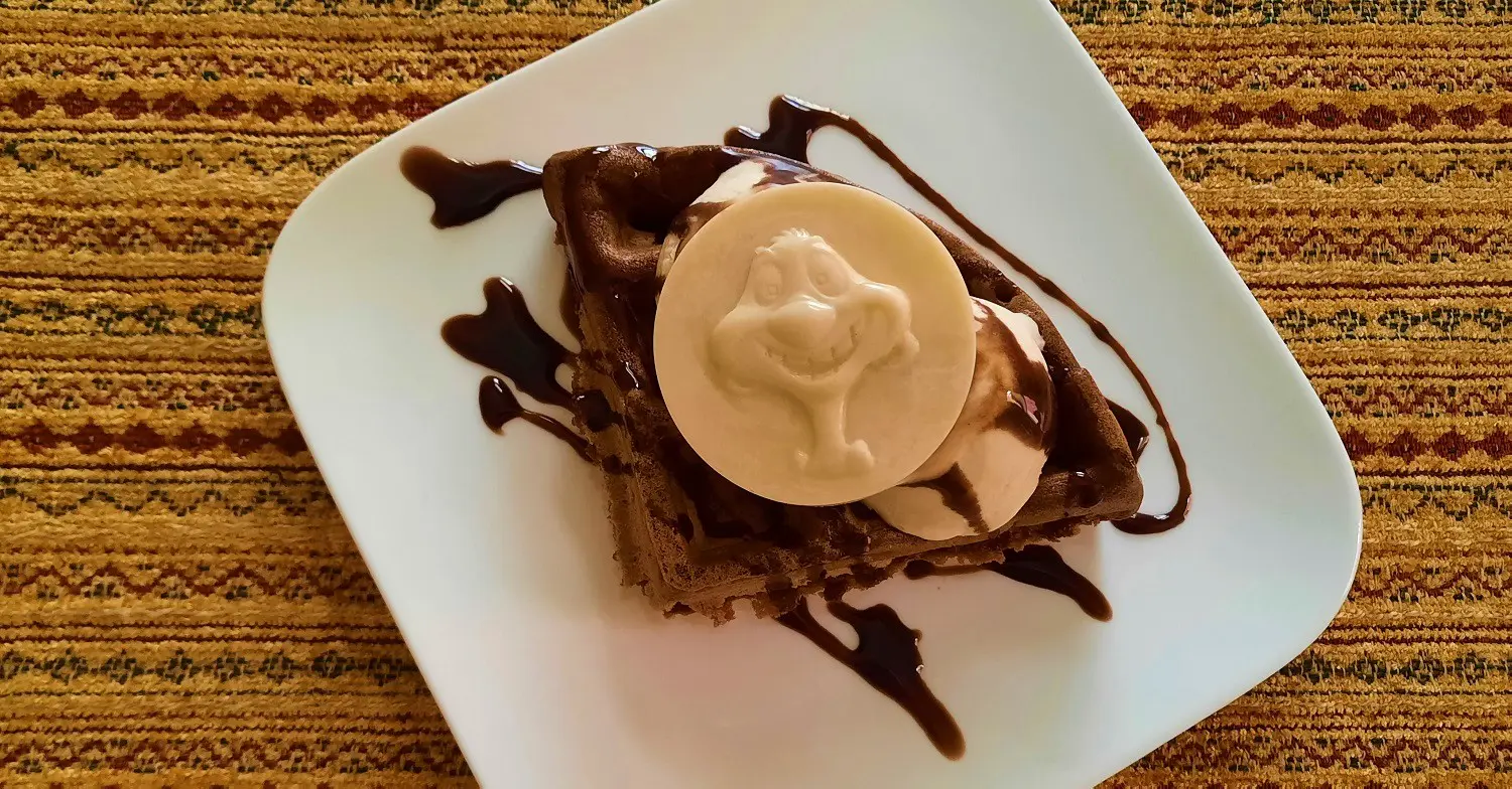 Schokoladenwaffel Auf einem weißen quadratischen Teller liegt eine Schokoladenwaffel mit gefrorener Espresso-Mousse und einem Täfelchen aus weißer Schokolade mit Timon-Motiv