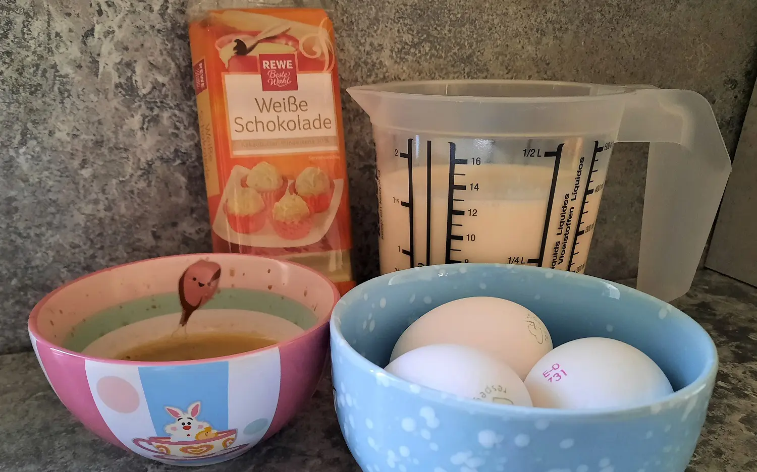 Zutaten für Espresso-Mousse Schlagsahne, weiße Schokolade, Eier und frischer Espresso sind in Gefäßen auf einer Küchenarbeitsfläche sichtbar
