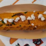 In einer Bambusschale liegt ein gegrillter Maiskolben mit Bröseln von veganem Feta obenauf