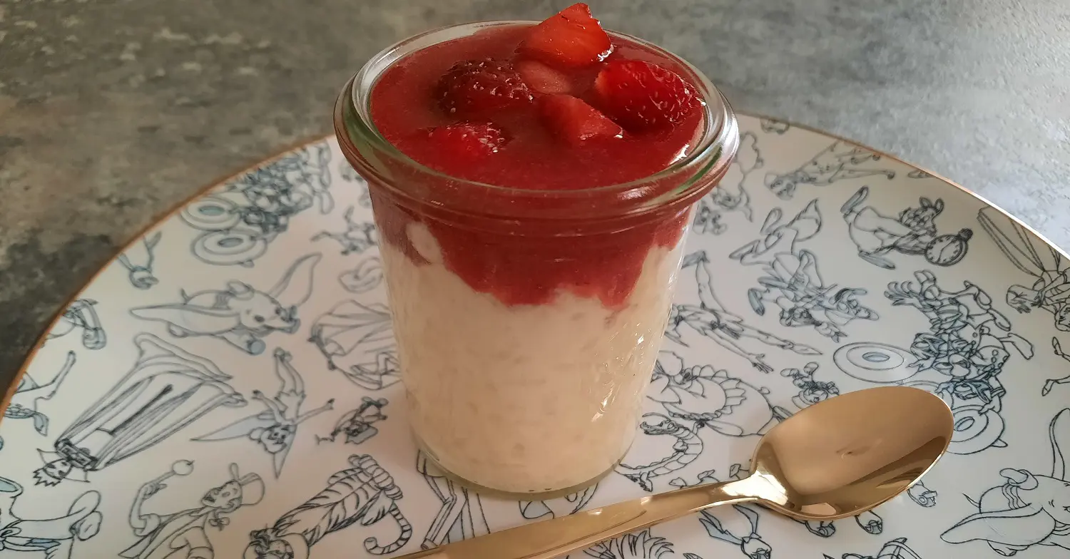 Rice Cream mit Erdbeeren Auf einem Teller mit Disney-Motiven steht ein kleines Glasgefäß mit süßer Reiscreme und Erdbeersauce
