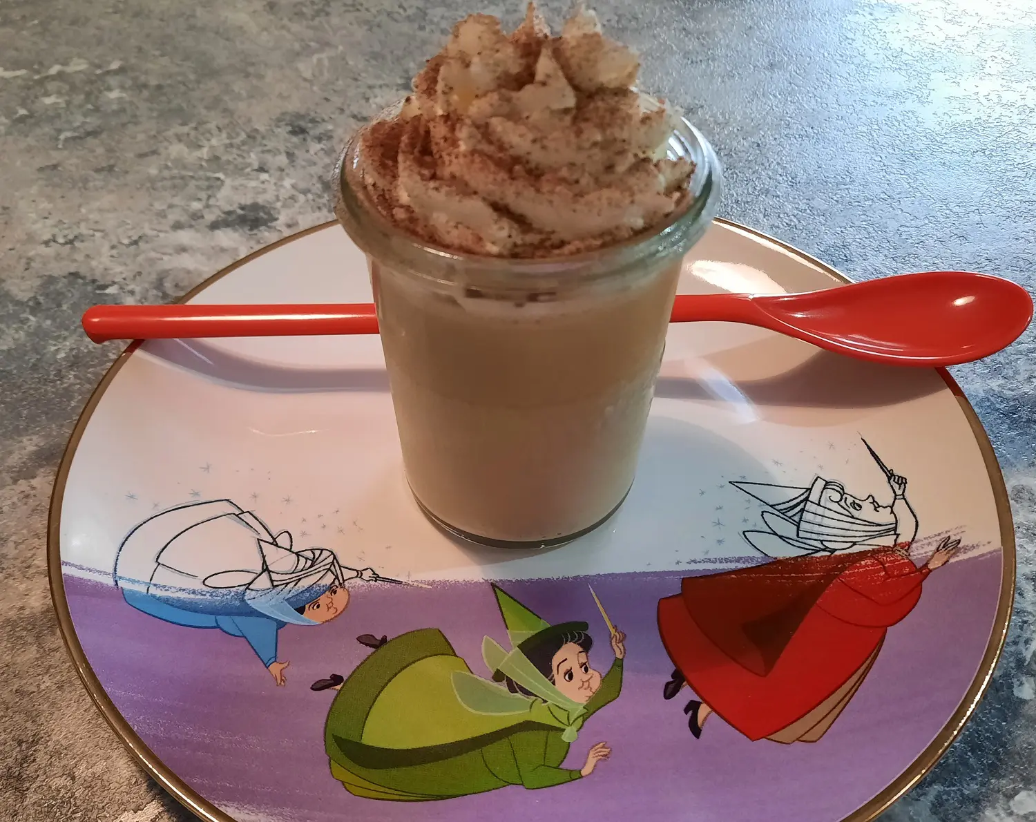 Frappuccino Cream Dessert Nachtisch in einem Dessertglas mit langem rotem Löffel auf einem Dessertteller mit Disney Motiv