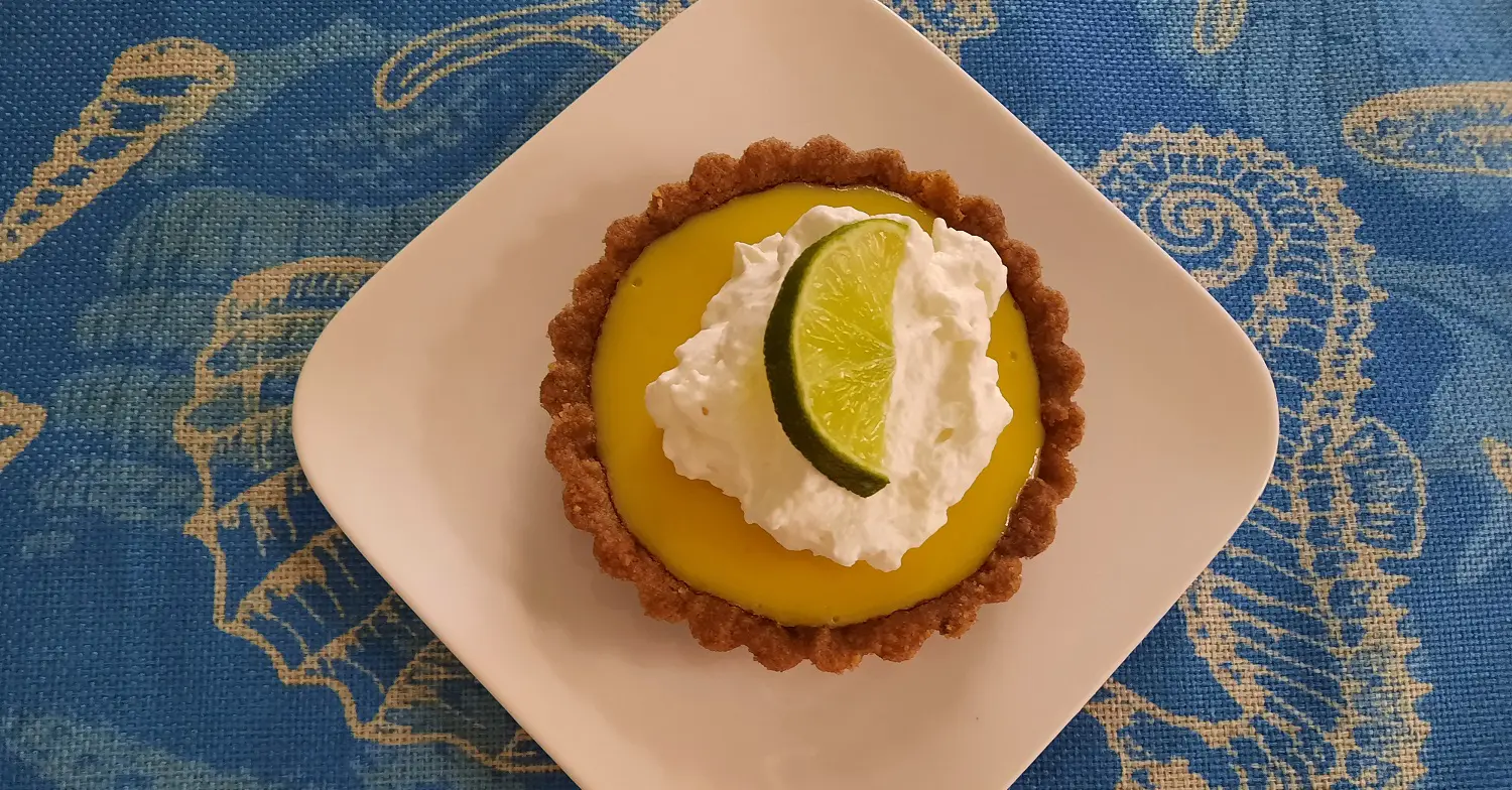 Key Lime Pie mit Sahne Ein Limettentörtchen auf einem quadratischen weißen Teller
