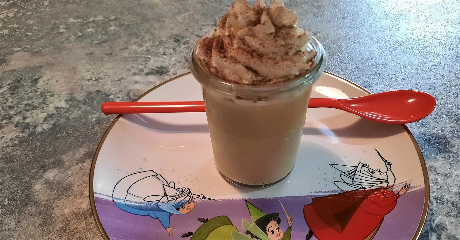 Ein Dessertglas mit Kaffee-Karamell-Dessert auf einem Teller mit Abbildung der drei Feen aus Dornröschen