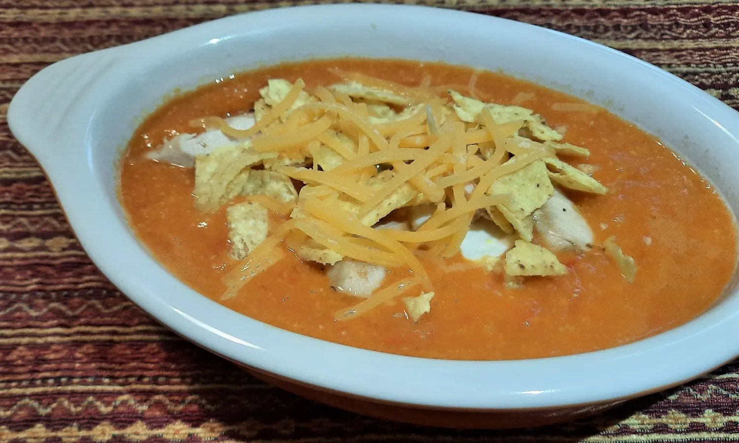 Schale mit Chicken Tortilla Soup Suppe garniert mit Tortilla Chips, Hähnchenstreifen und Cheddar