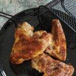 Drei Hähnchenflügel mit Marinade auf einem schwarzen Teller