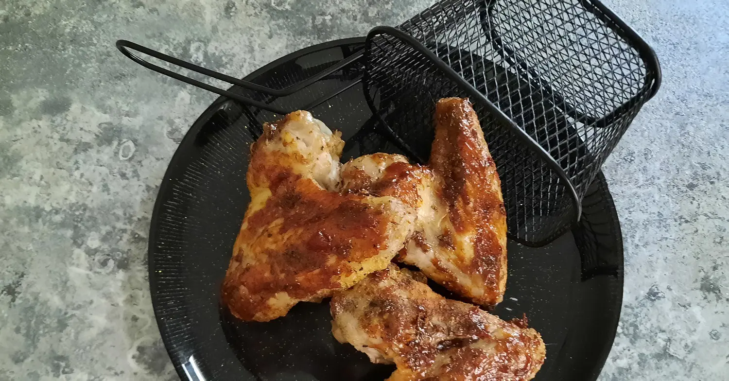 Knusprige Hähnchenschenkel Drei Hähnchenflügel mit Marinade auf einem schwarzen Teller