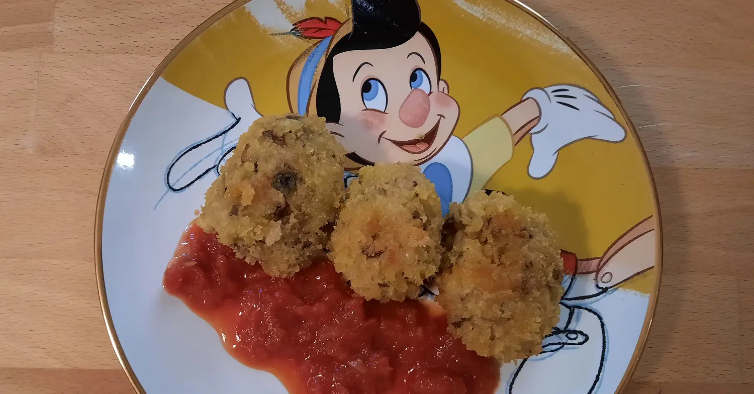 Teller mit drei Arancini Drei frittierte Risottobällchen sind mit Tomatensauce auf einem Teller mit Pinocchio-Motiv angerichtet