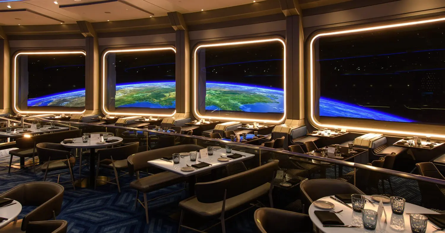 Restaurant Space 220 Gastraum Blick in den Gastraum mit Tischen und Stühlen sowie dem Blick in den Weltraum in Richtung Erde