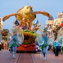 Tänzerinnen mit bunten Muschelkostümen schreiten vor dem Crush Paradewagen voran