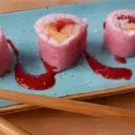 Frucht-Sushi auf einer türkisblauen Servierplatte angerichtet mit Essstäbchen