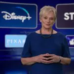 Christine McCarthy in einem dunkelblauen Kleid vor einem Bildschirm mit Disney Plus Einblendungen