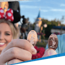 Zwei Personen halten Pressed Pennies vor dem Cinderella Castle in Richtung Kamera