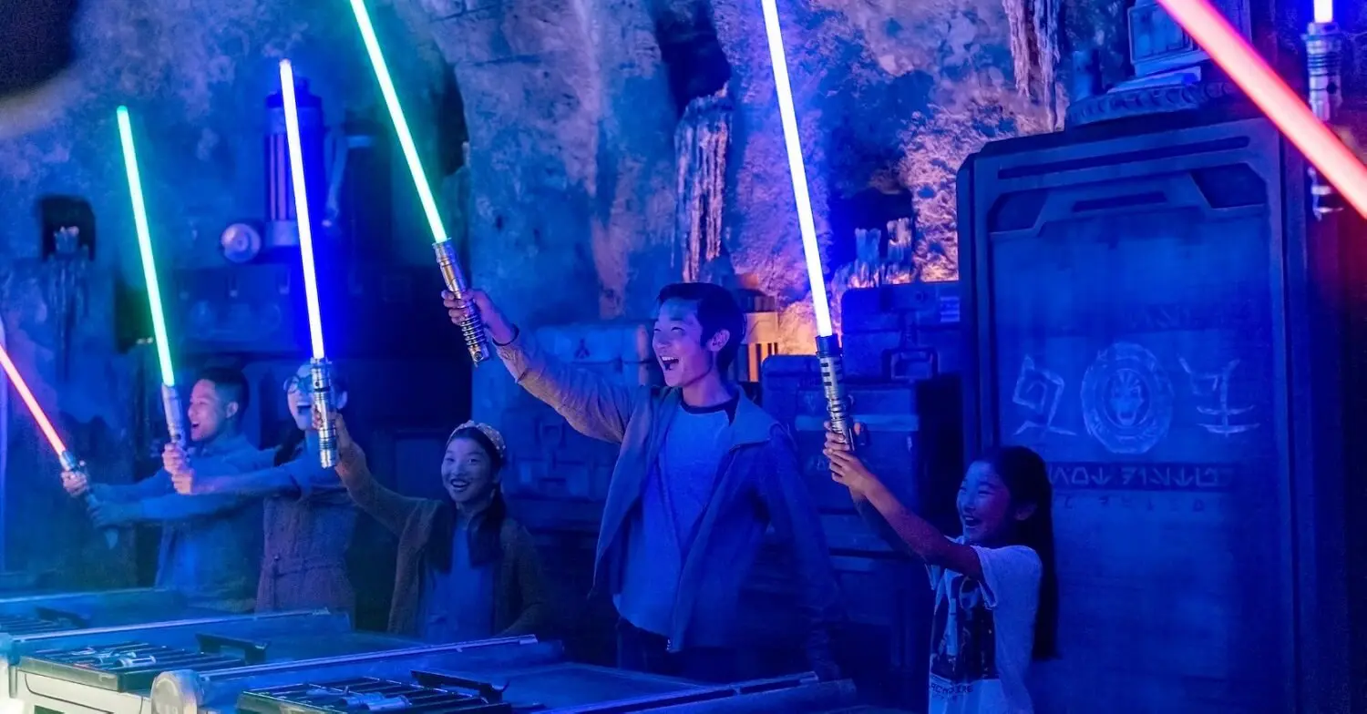 Besucher halten in Savis Workshop in Galaxys Edge leuchtende Lichtschwerter in die Luft