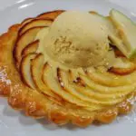 Tarte Tartin mit einer Kugel Vanilleeis, die langsam schmilzt und zwei frischen Apfelspalten