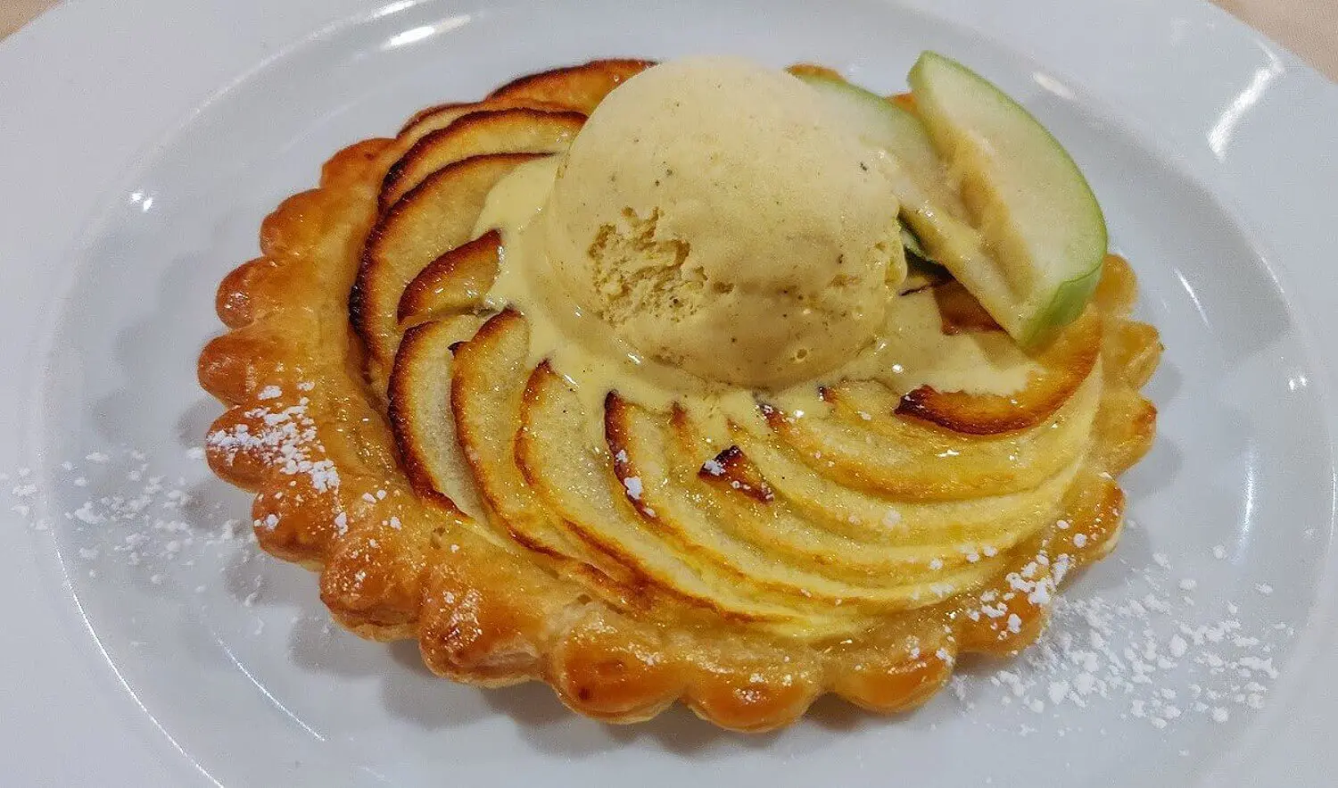 Tarte Tartin Tarte Tartin mit einer Kugel Vanilleeis, die langsam schmilzt und zwei frischen Apfelspalten