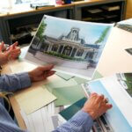 Zwei Imagineers betrachten ein Concept Art für den renovierten Eingangsbereich des Plaza Gardens Restaurants in DIsneyland Paris. Auf dem Schreibtisch liegen weitere Fotos des Restaurants