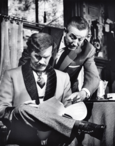 Walt Disney beugt sich über den lebensgroßen Audio Animatronic von Vater John und schaut mit ihmgemeinsam auf ein Skript oder Dokument, als würde er mit einem echten Schauspieler Text durchgehen.