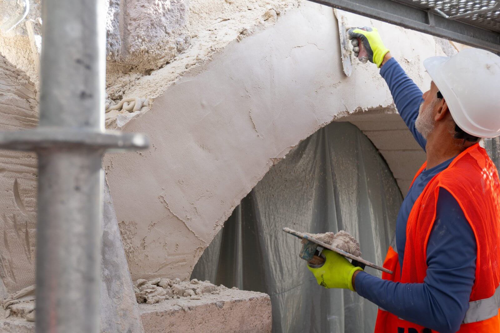 Handwerker mit Helm glättet Putz an einem Bogen der Brücke zum Dornröschenschloss zwischen Baugerüsten