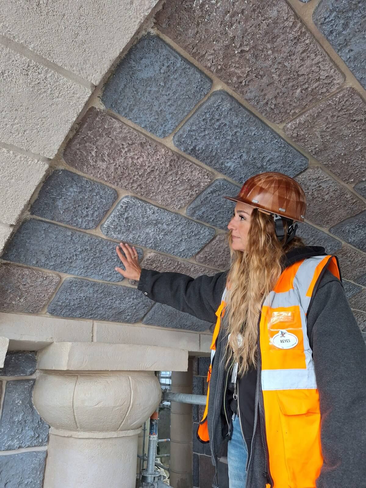Mitarbeiterin mit Schutzhelm zeigt die handbemalten Kunststeine an der Bogenunterseite der Schlossbrücke