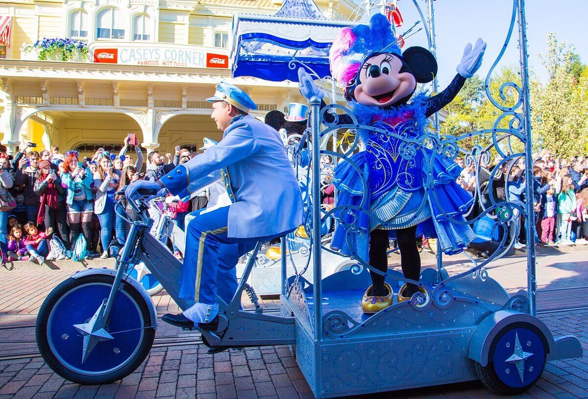 Minnie mouse in ihrem hellblauen Ballkeldi speziell für den 25. Geburtstag von Disneyland Paris, steht auf dem Anhänger eines Tricycles und wird über die Main Street, U.S.A. gefahren