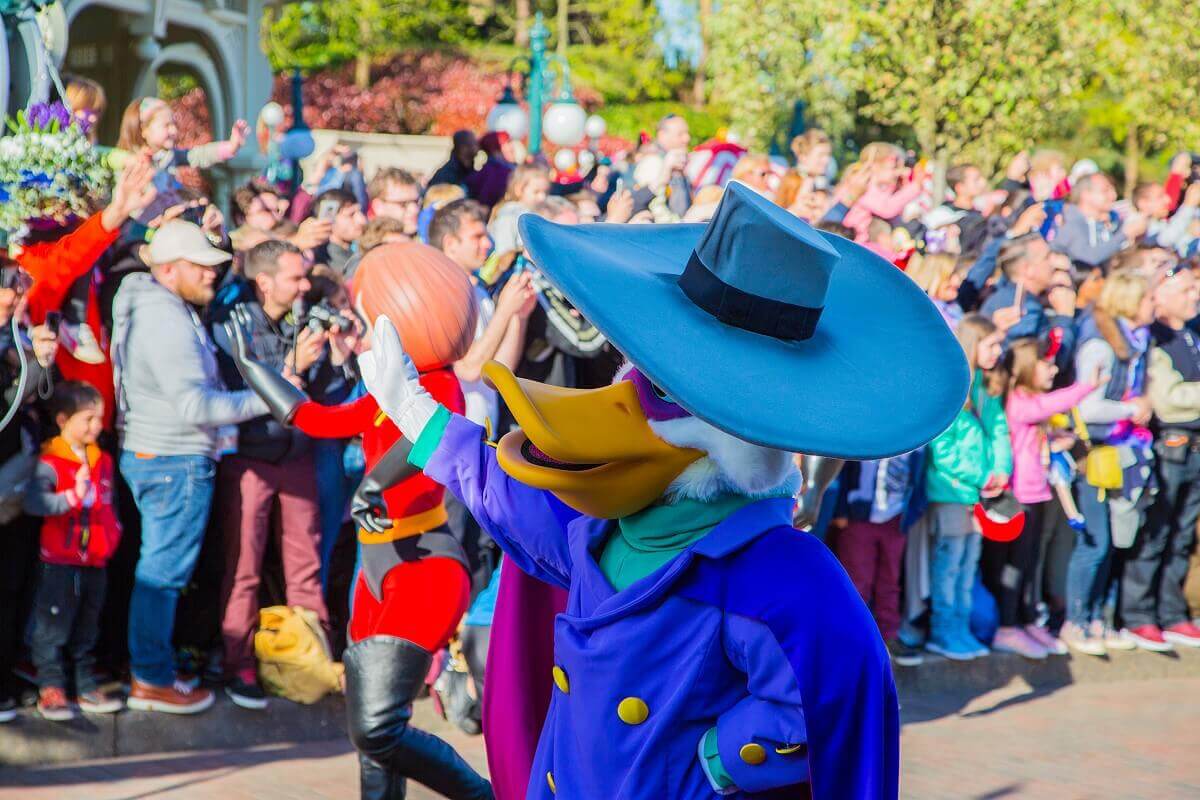 Die Ente Darkwing Duck läuft neben Mrs Incredible winkend an den Paradenzuschauern vorbei