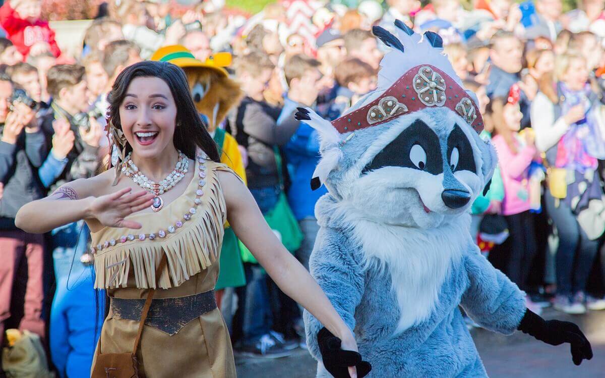 Pocahontas tanzt Hand in Hand mit Meeko über die Main Street, U.S.A. Meeko trägt einen Indianerkopfschmuck