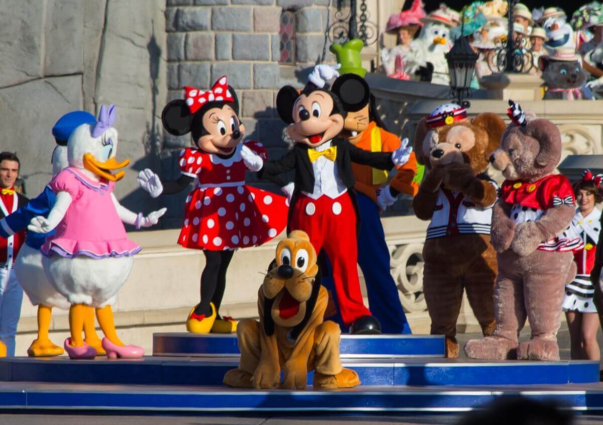 Pluto hockt vor Mickey und Minnie, links im Bild sind Daisy Duck und Donald zu sehen, rechts im Bild Duffy der Disney Bär und Shellie May