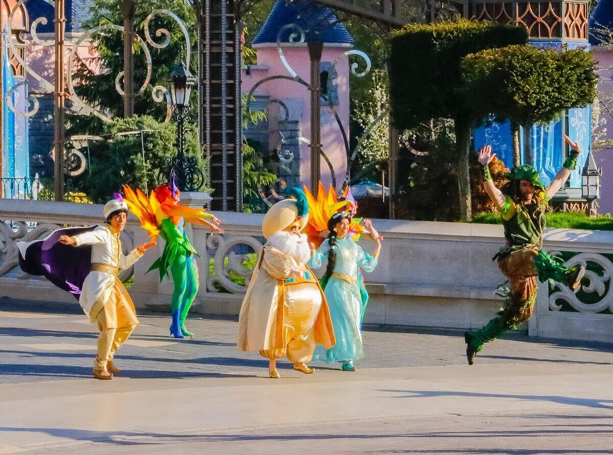 Jasmin geht Hand mit Hand mit ihrem Vater, dem Sultan, daneben Aladdin. Sie werden von bunt gekleideten Tänzern begleitet
