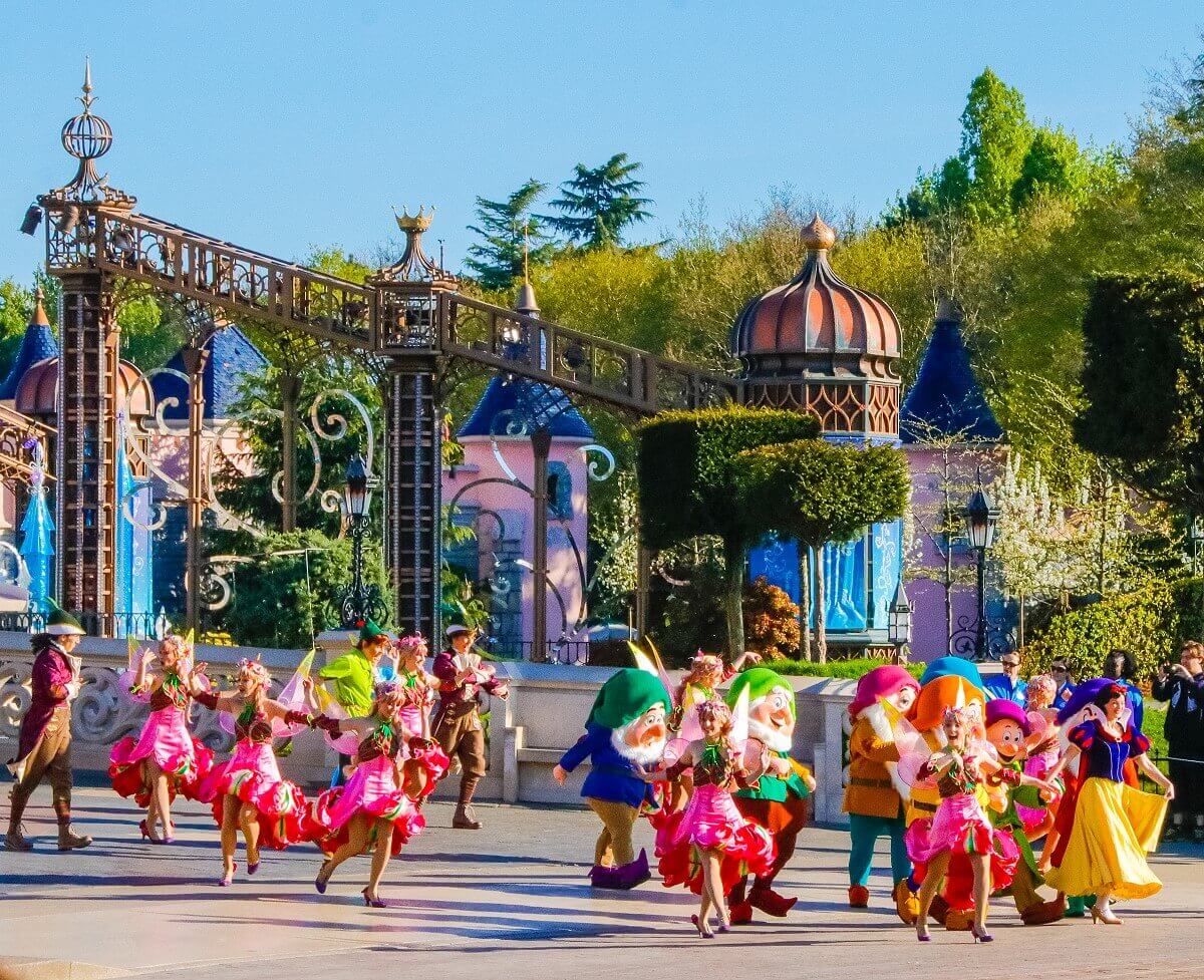 Auf der Brücke vor dem Schloss sind Schneewittchen und die sieben Zwerge zu sehen, außerdem Peter Pan und jede Menge Tänzerinnen und Tänzer in märchenhaften Kostümen