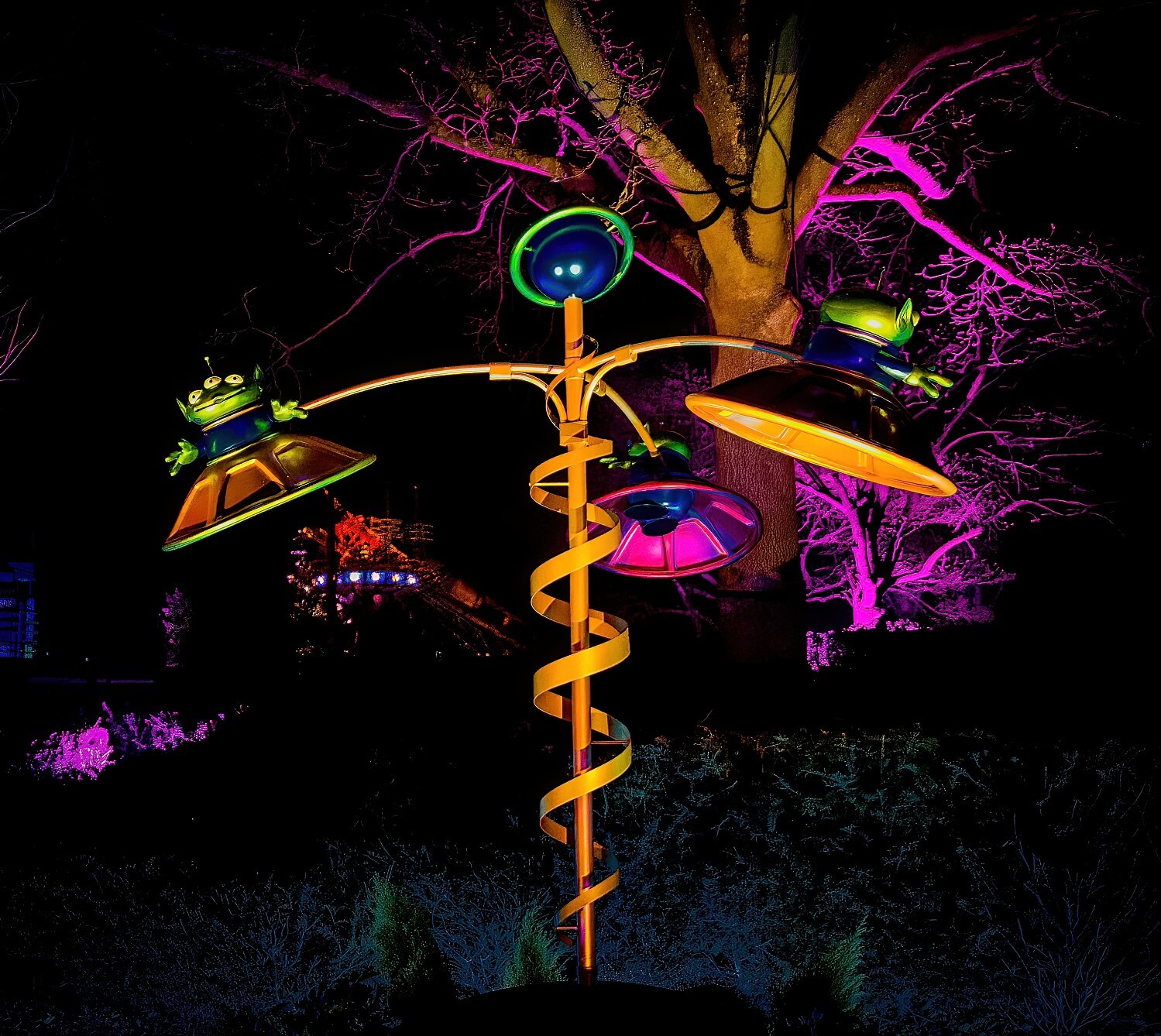 Blick auf die Toy Story Skulptur in den Gardens of Wonder bei Nacht: drei grüne Aliens sitzen in fliegenden Untertassen und umkreisen einen Planeten