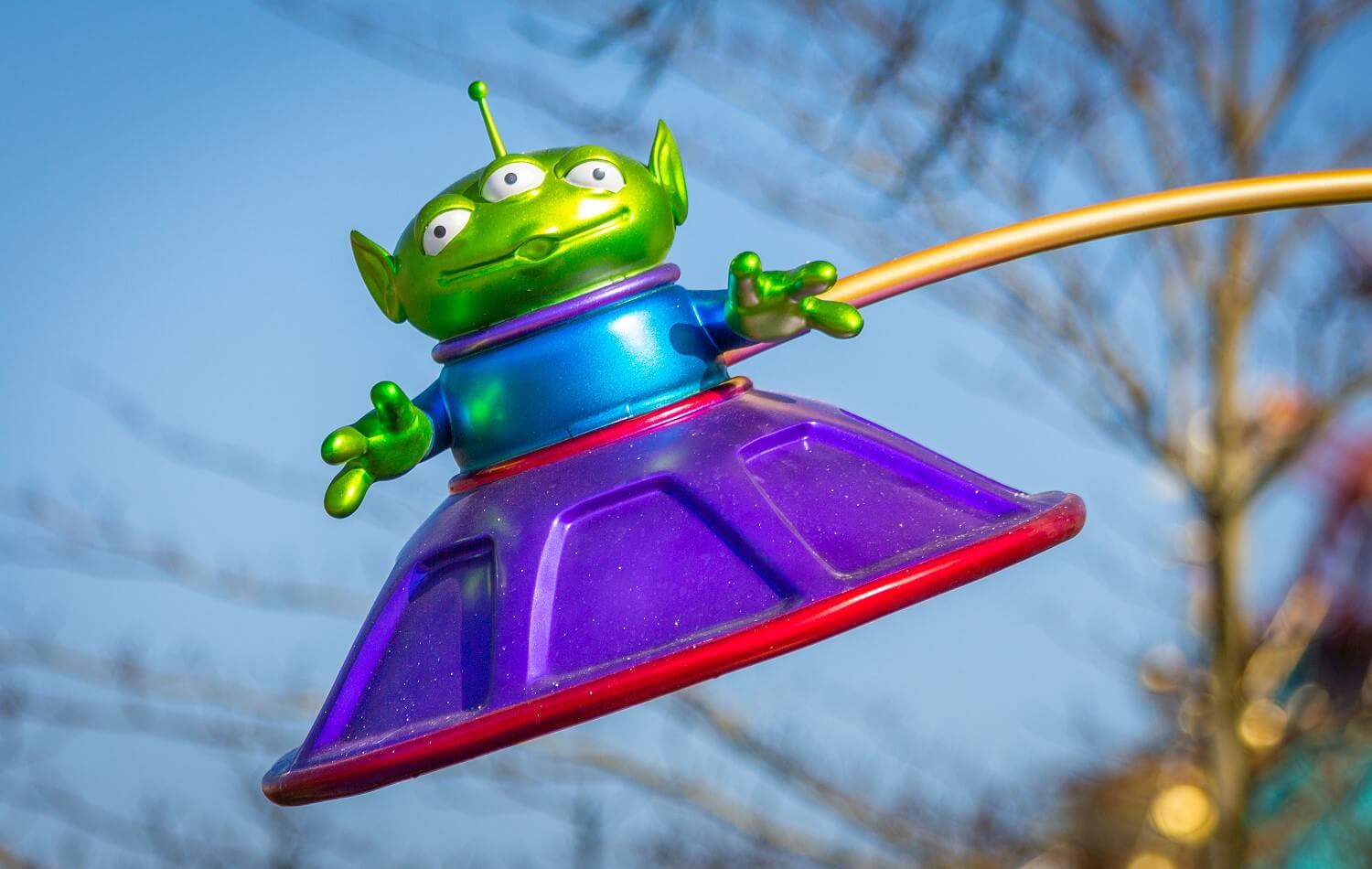Grünes Toy Story Alien mit drei Augen in einer lilafarbenden fliegenden Untertasse